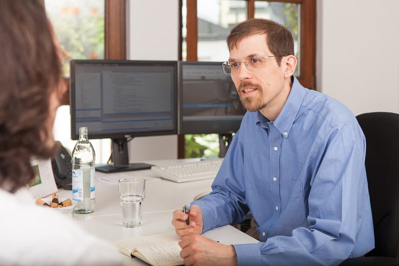 Beratungsgespräch am Schreibtisch mit zwei Monitoren